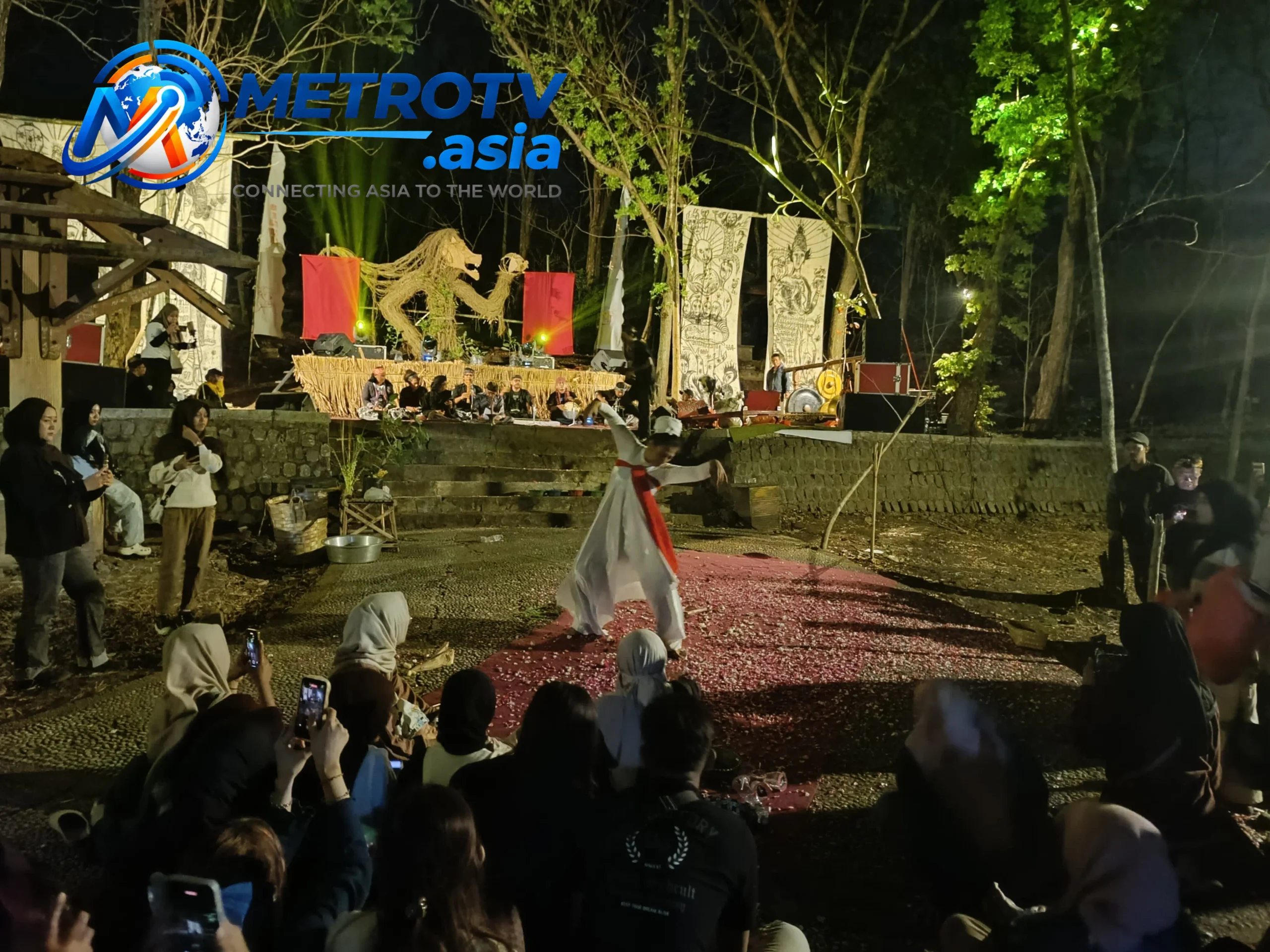 Penari berbusana putih dengan selendang merah menampilkan tarian di atas hamparan kelopak bunga, penonton merekam momen tersebut pada acara Waringin Sasmita 2 Goa Selomangleng Kediri